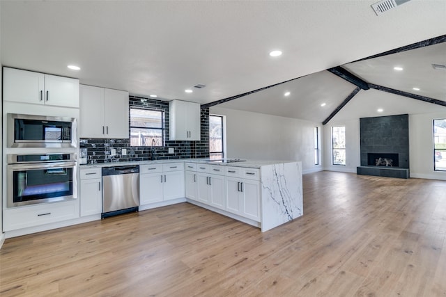 kitchen with white cabinetry, vaulted ceiling with beams, light stone countertops, and stainless steel appliances