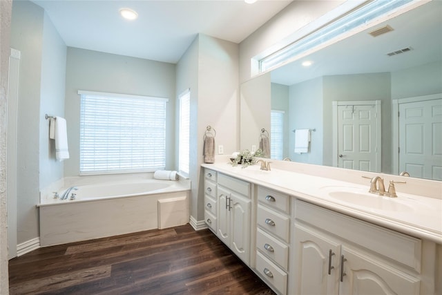 full bath featuring double vanity, visible vents, a sink, wood finished floors, and a bath