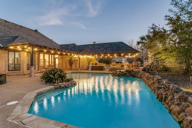 pool at dusk featuring a patio, exterior kitchen, and an outdoor pool