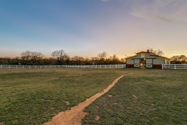 yard at dusk featuring a rural view, fence, and a barn