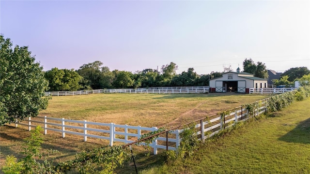 view of yard with a detached garage, fence, an outbuilding, and a rural view