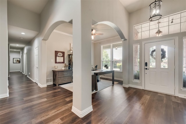 entryway with arched walkways, dark wood-style floors, and baseboards