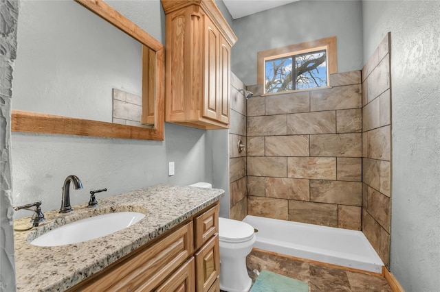 full bathroom featuring a stall shower, a textured wall, vanity, and toilet