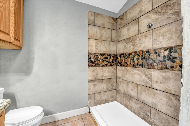 full bathroom featuring toilet, baseboards, tiled shower, and tile patterned floors