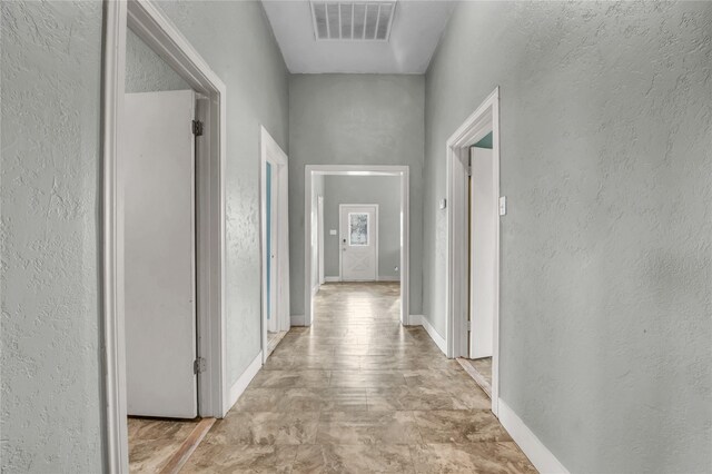 hallway with a textured wall, visible vents, and baseboards