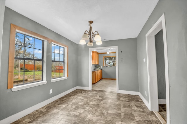 unfurnished dining area featuring baseboards, a healthy amount of sunlight, and an inviting chandelier