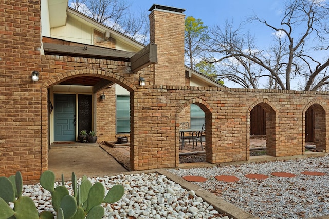 view of side of home with brick siding, a chimney, and a patio