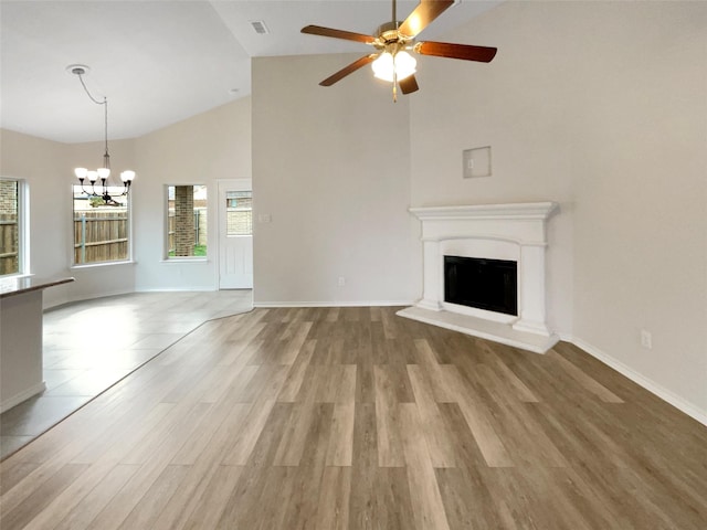 unfurnished living room featuring a fireplace with raised hearth, high vaulted ceiling, ceiling fan with notable chandelier, and light wood-style flooring