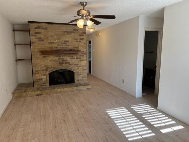 unfurnished living room featuring a fireplace, a textured ceiling, ceiling fan, and light hardwood / wood-style flooring