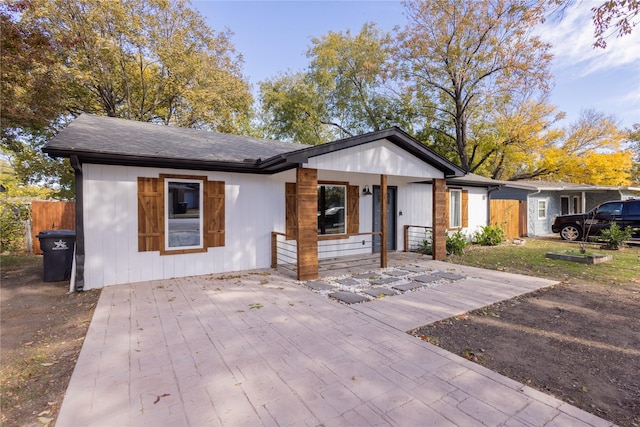 view of front facade featuring covered porch, a shingled roof, fence, and concrete driveway