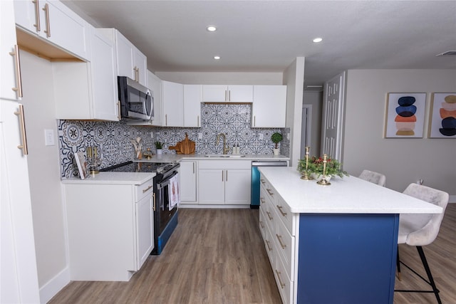 kitchen featuring a breakfast bar, stainless steel microwave, black range with electric stovetop, a sink, and dishwashing machine