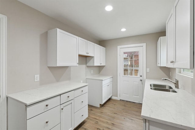 kitchen featuring light stone countertops, light wood-type flooring, white cabinetry, a sink, and recessed lighting