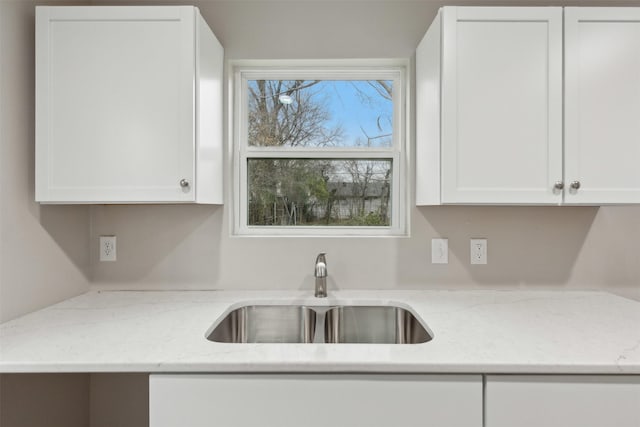 kitchen featuring built in study area, a sink, light stone countertops, and white cabinets