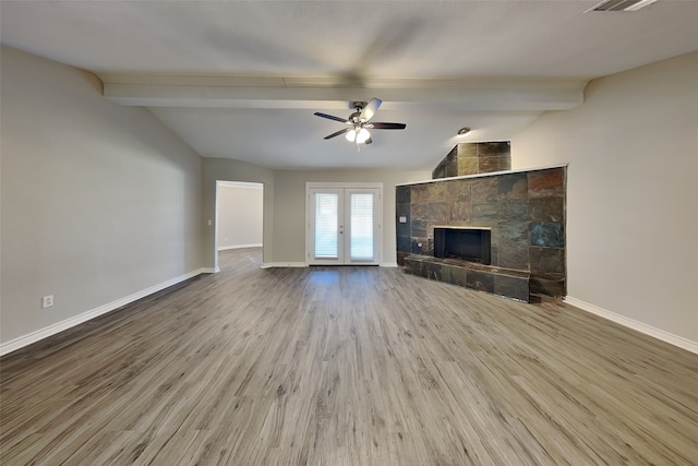 unfurnished living room with lofted ceiling with beams, a tile fireplace, light hardwood / wood-style floors, ceiling fan, and french doors