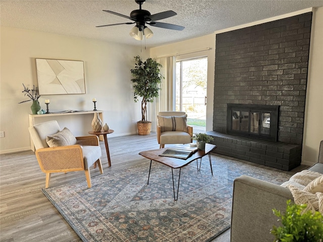 living room featuring a fireplace, light hardwood / wood-style flooring, a textured ceiling, and ceiling fan