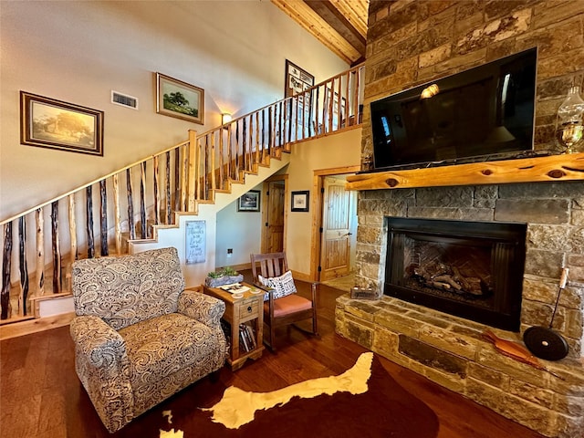 living room featuring beam ceiling, wood-type flooring, a towering ceiling, and a fireplace