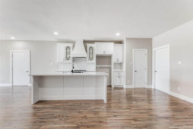 kitchen with white cabinetry, a center island with sink, custom exhaust hood, and backsplash