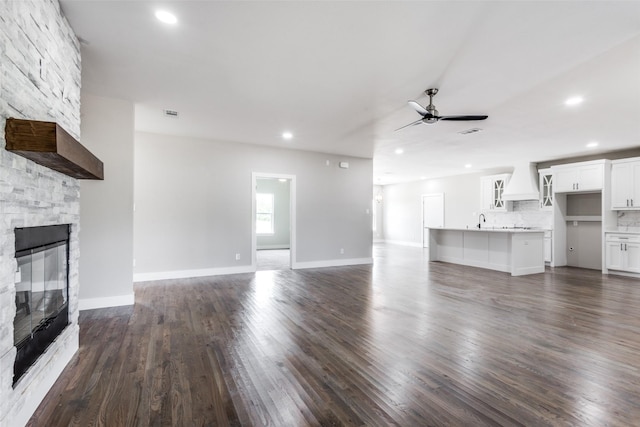 unfurnished living room featuring sink, ceiling fan, dark wood-type flooring, and a fireplace