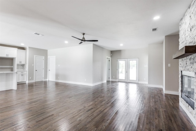 unfurnished living room featuring ceiling fan, french doors, dark wood-type flooring, and a stone fireplace