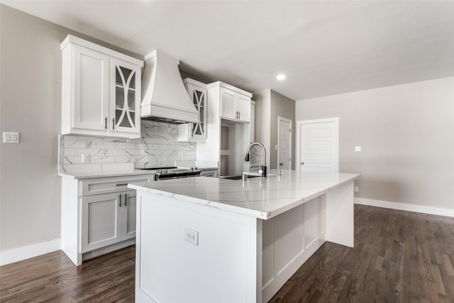 kitchen with white cabinetry, a kitchen island with sink, sink, tasteful backsplash, and custom range hood