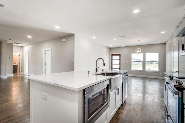 kitchen featuring an island with sink, stainless steel appliances, light stone counters, dark hardwood / wood-style floors, and pendant lighting