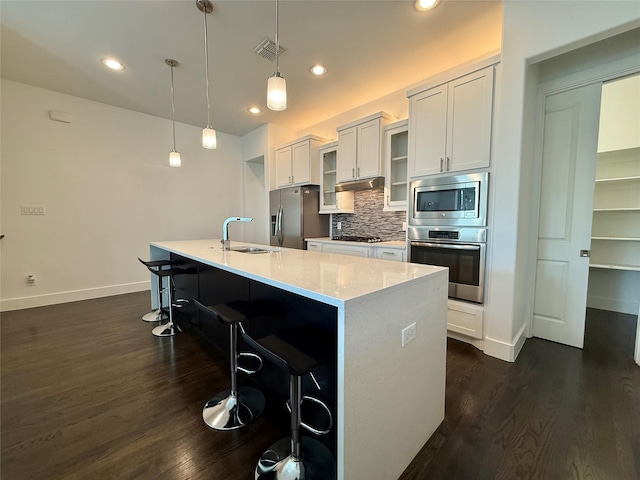 kitchen with an island with sink, white cabinetry, decorative light fixtures, sink, and appliances with stainless steel finishes