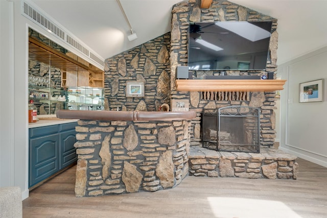 living room featuring lofted ceiling, rail lighting, a stone fireplace, and wood finished floors