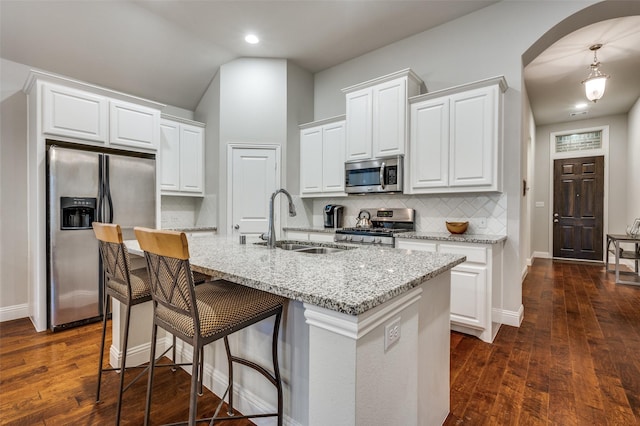 kitchen with a center island with sink, light stone countertops, stainless steel appliances, white cabinetry, and pendant lighting