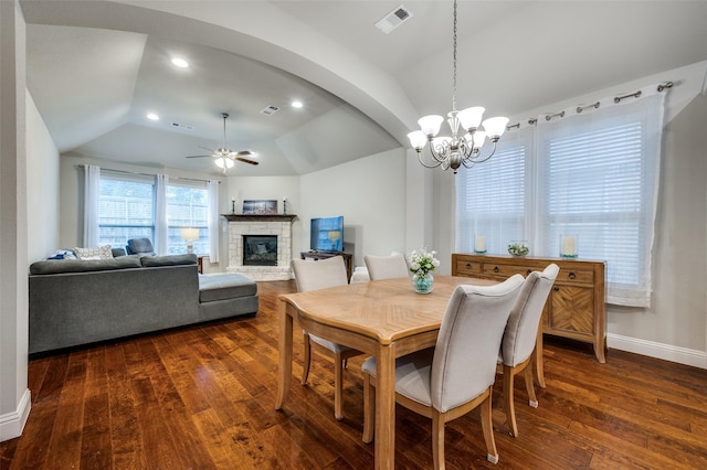 dining space with visible vents, dark wood-type flooring, vaulted ceiling, a fireplace, and ceiling fan with notable chandelier