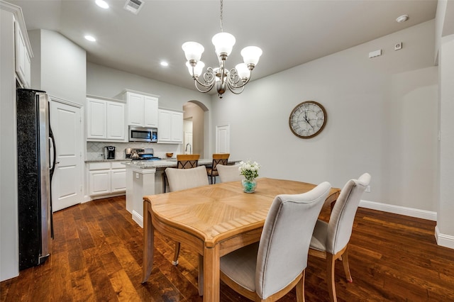 dining space with arched walkways, a notable chandelier, visible vents, baseboards, and dark wood finished floors