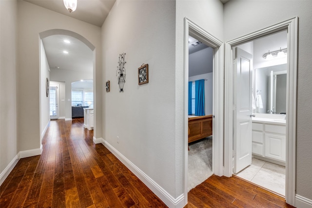 hallway featuring baseboards, arched walkways, and wood finished floors