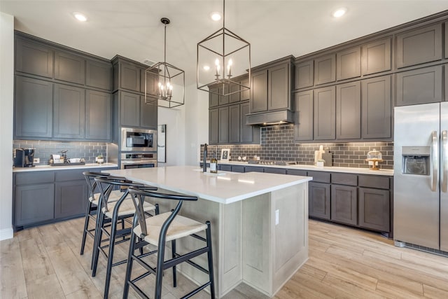 kitchen featuring stainless steel appliances, light countertops, light wood-style flooring, and an island with sink