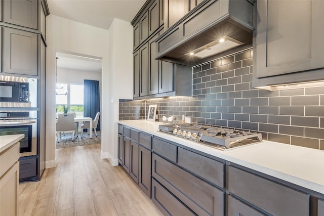 kitchen with custom range hood, stainless steel appliances, backsplash, and light countertops