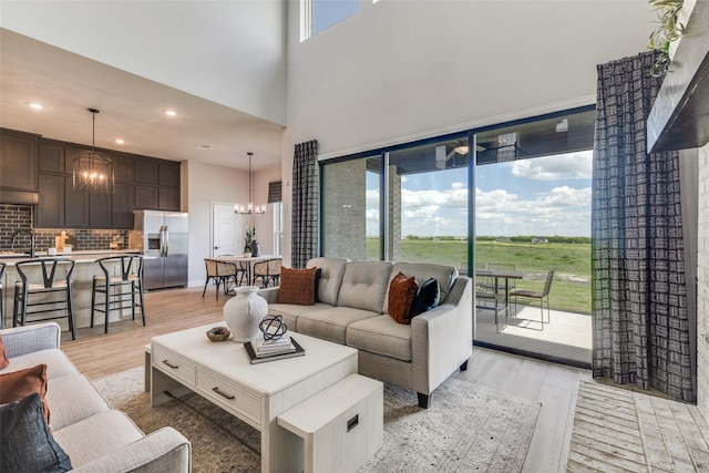 living room featuring a high ceiling, recessed lighting, light wood-style flooring, and an inviting chandelier