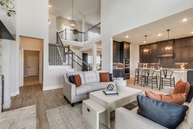 living room featuring light wood finished floors, baseboards, stairway, and a notable chandelier