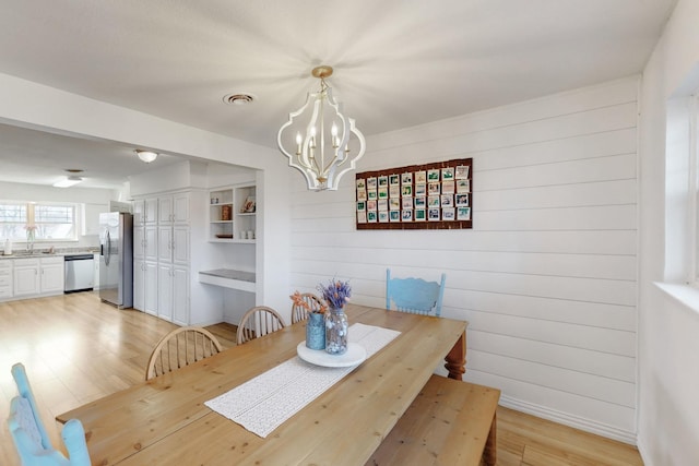 dining area featuring a notable chandelier, sink, light hardwood / wood-style floors, and wood walls