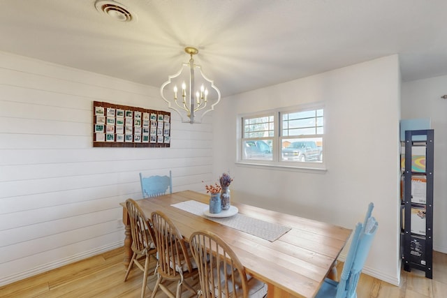 dining space with wood walls, a chandelier, and light hardwood / wood-style floors