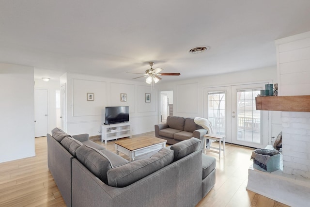 living room featuring a brick fireplace, light hardwood / wood-style flooring, ceiling fan, and french doors