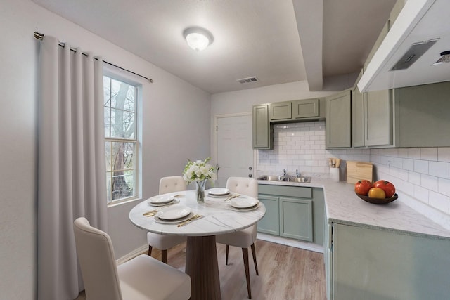 kitchen with sink, light stone counters, light hardwood / wood-style floors, green cabinetry, and tasteful backsplash