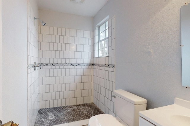 bathroom featuring a tile shower, vanity, and toilet