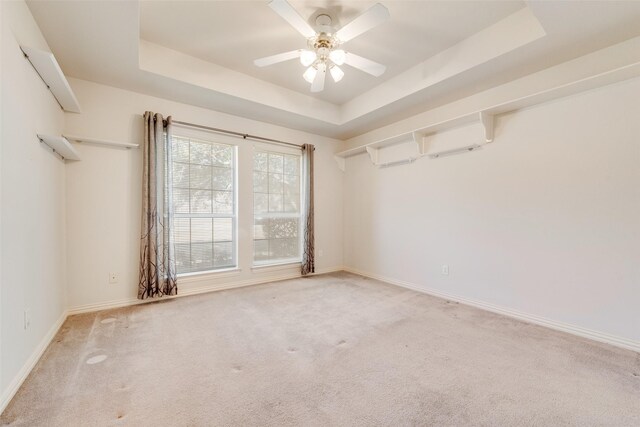 empty room featuring carpet floors, a raised ceiling, a ceiling fan, and baseboards