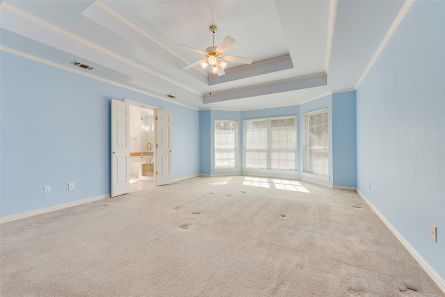 unfurnished room with a tray ceiling, visible vents, light colored carpet, ornamental molding, and baseboards