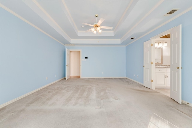 unfurnished bedroom with a tray ceiling, light colored carpet, visible vents, ensuite bathroom, and baseboards