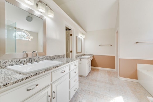 bathroom featuring baseboards, two vanities, a sink, and a tub