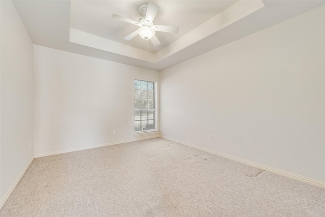 empty room with baseboards, a raised ceiling, a ceiling fan, and light colored carpet