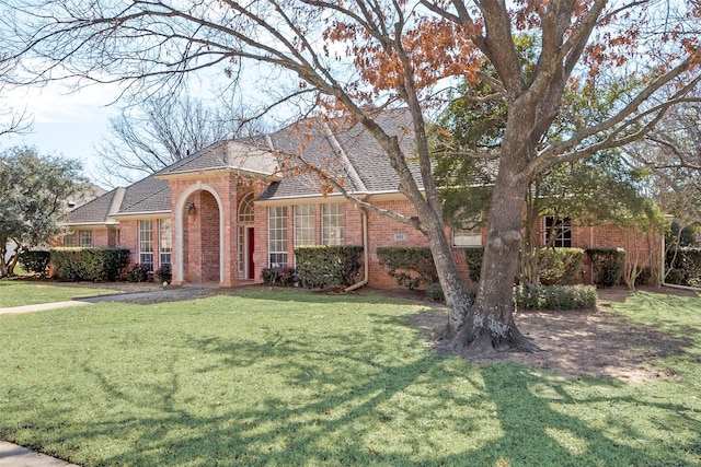 view of front of house with a shingled roof, a front yard, and brick siding