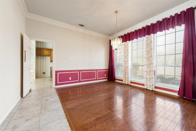 empty room featuring ornamental molding, light wood-type flooring, wainscoting, and visible vents