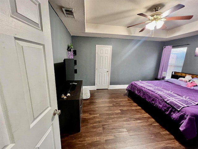 bedroom with a raised ceiling, ceiling fan, and dark hardwood / wood-style floors