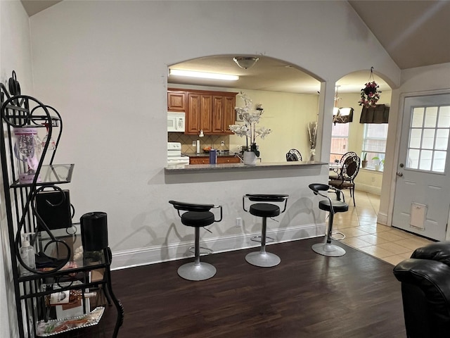 kitchen with white appliances, light tile patterned floors, vaulted ceiling, backsplash, and kitchen peninsula