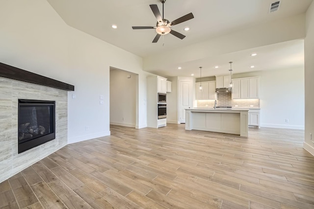 unfurnished living room with light wood-type flooring, visible vents, baseboards, and a fireplace